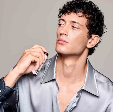 mann mit lockigen dunklen haar sprüht sich mit den olfazeta taschenparfum auf seinen hals